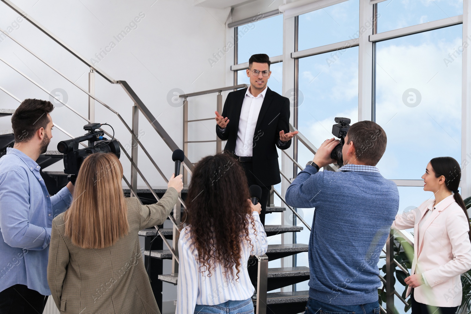 Photo of Happy business man talking to group of journalists indoors