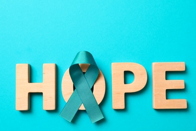 Photo of Word Hope made of wooden letters and teal awareness ribbon on light blue background. Symbol of social and medical issues