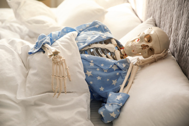 Photo of Human skeleton in pajamas lying on bed indoors