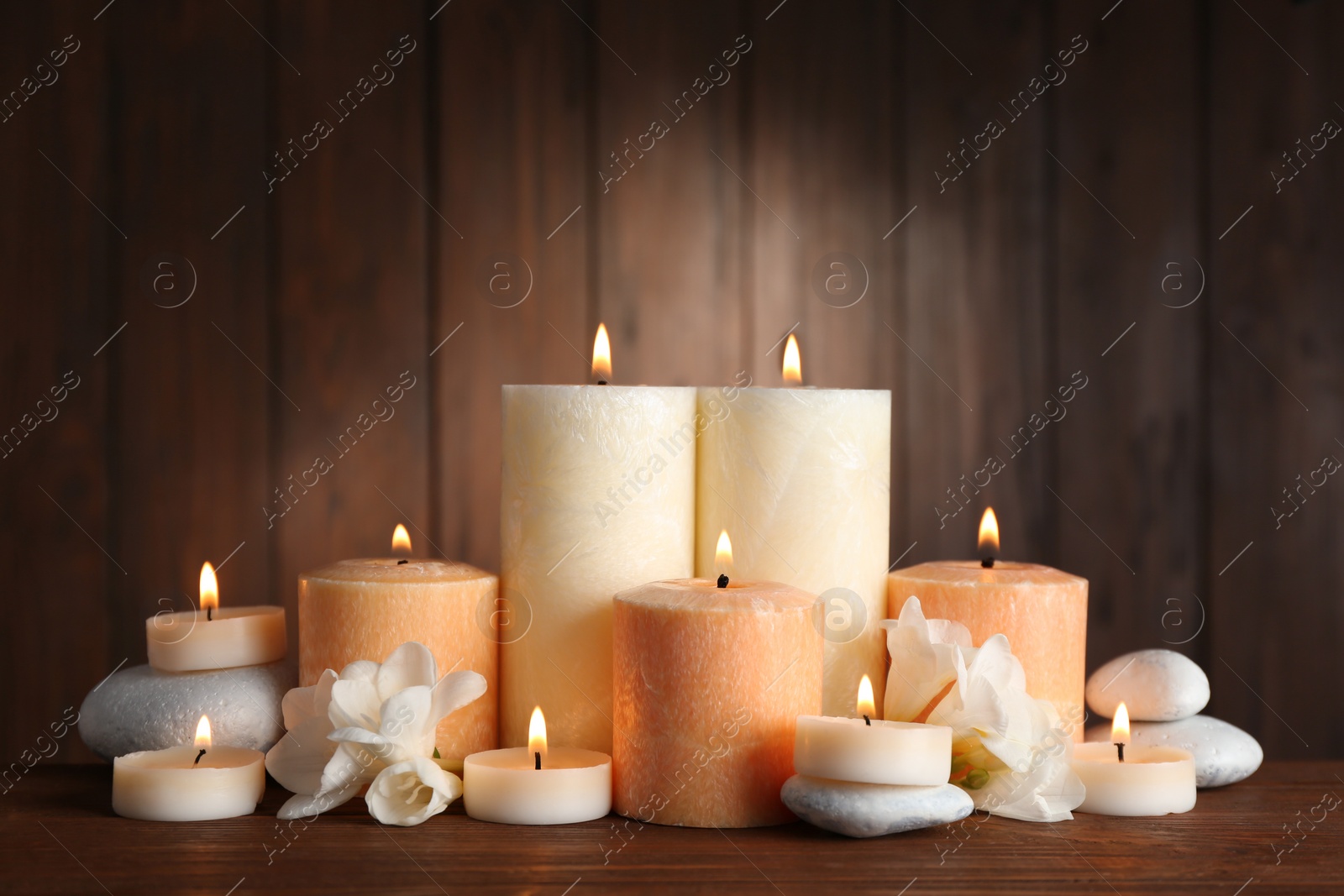 Photo of Beautiful composition with candles, flowers and stones on table against wooden background