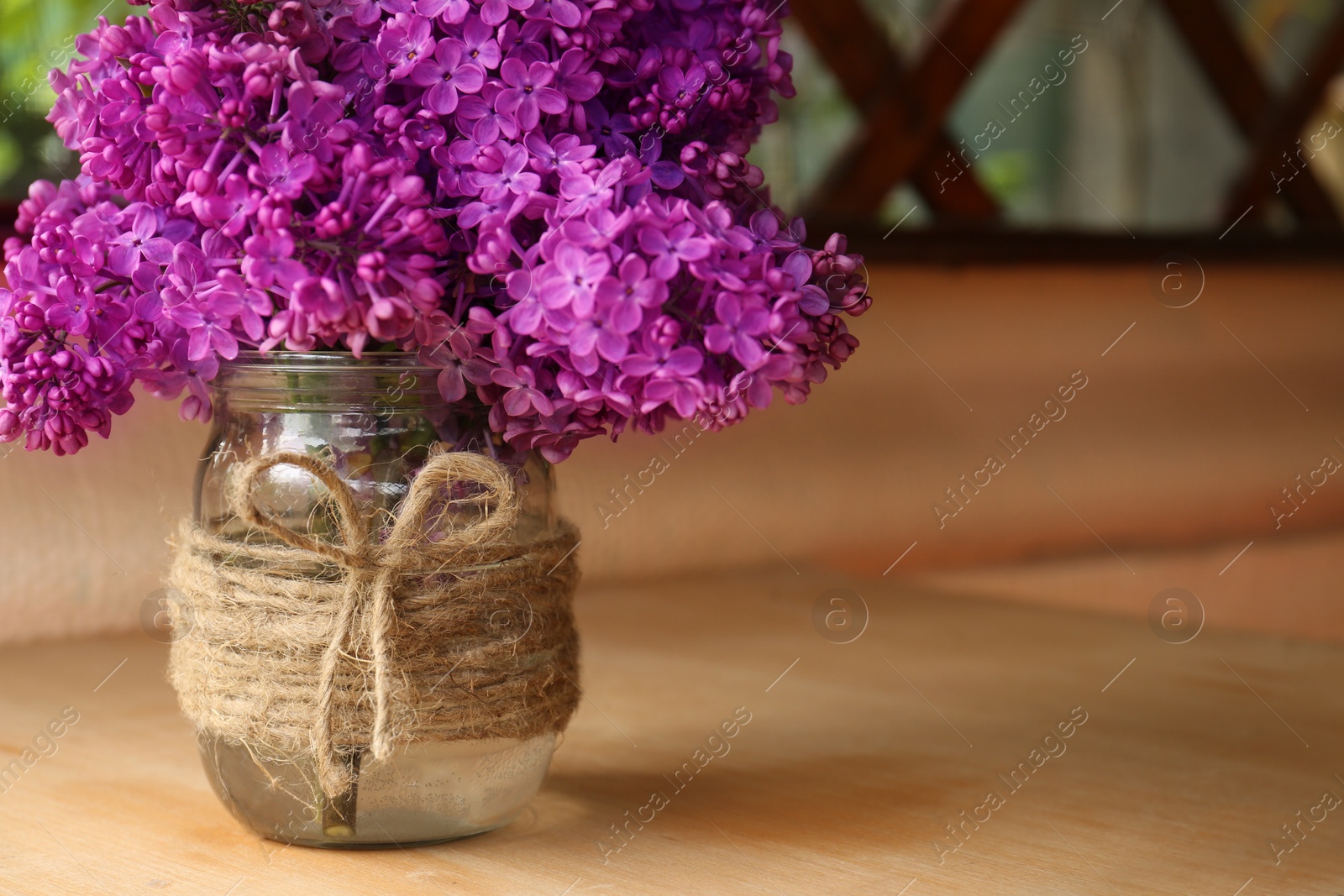 Photo of Beautiful lilac flowers in glass jar on wooden table indoors. Space for text