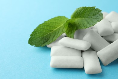 Photo of Pile of tasty white chewing gums and mint leaves on light blue background, closeup. Space for text