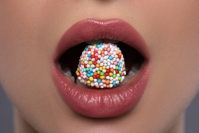 Photo of Woman with beautiful lips eating candy on grey background, closeup