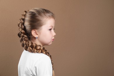 Little girl with braided hair on light brown background. Space for text