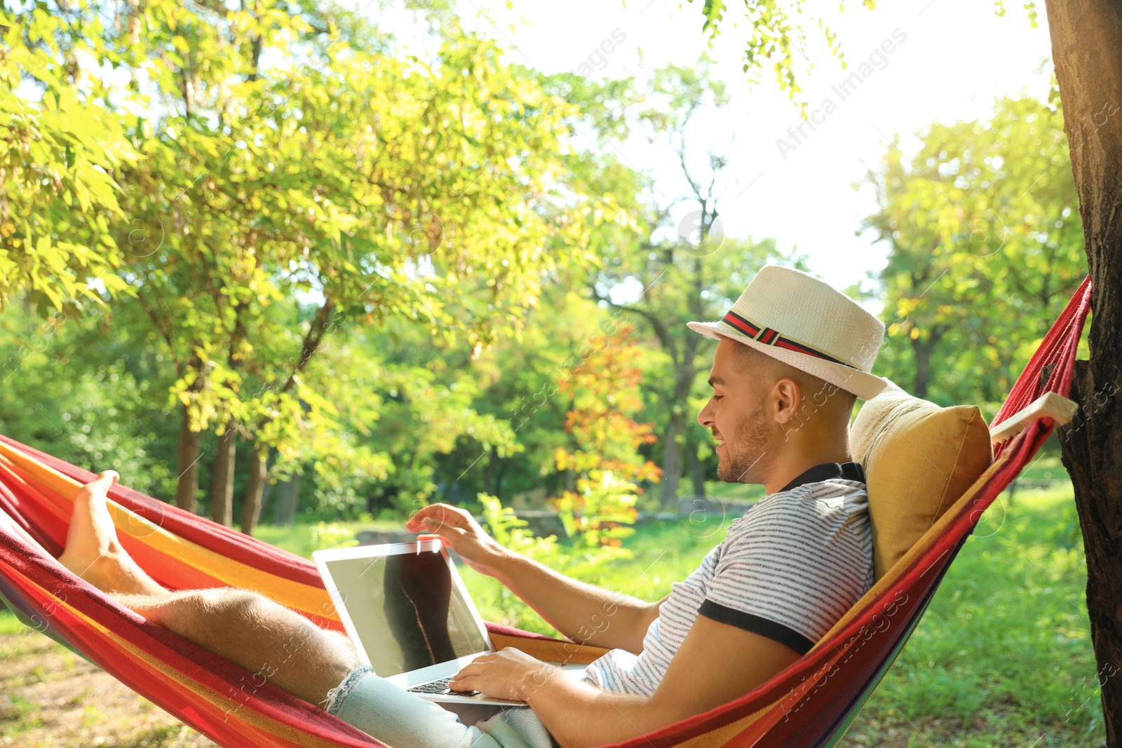 Photo of Young man with laptop resting in comfortable hammock at green garden