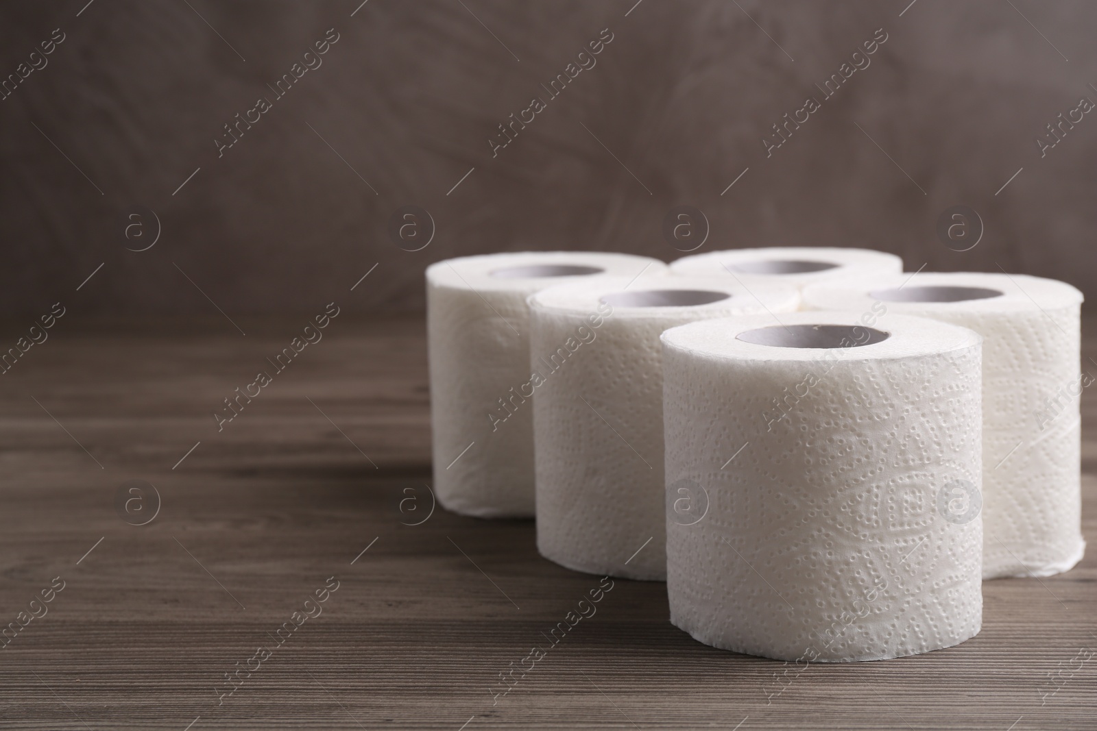 Photo of Soft toilet paper rolls on wooden table, closeup. Space for text