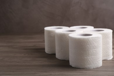 Photo of Soft toilet paper rolls on wooden table, closeup. Space for text