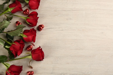 Beautiful red roses and heart shaped candies on white wooden background, flat lay with space for text. Valentine's Day celebration