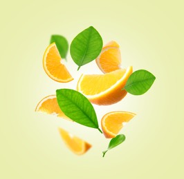 Image of Juicy orange slices and green leaves flying on cream background