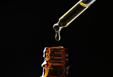 Photo of Dripping tincture from pipette into bottle on black background, closeup