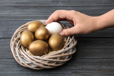 Photo of Woman taking egg from nest with gold ones on wooden table