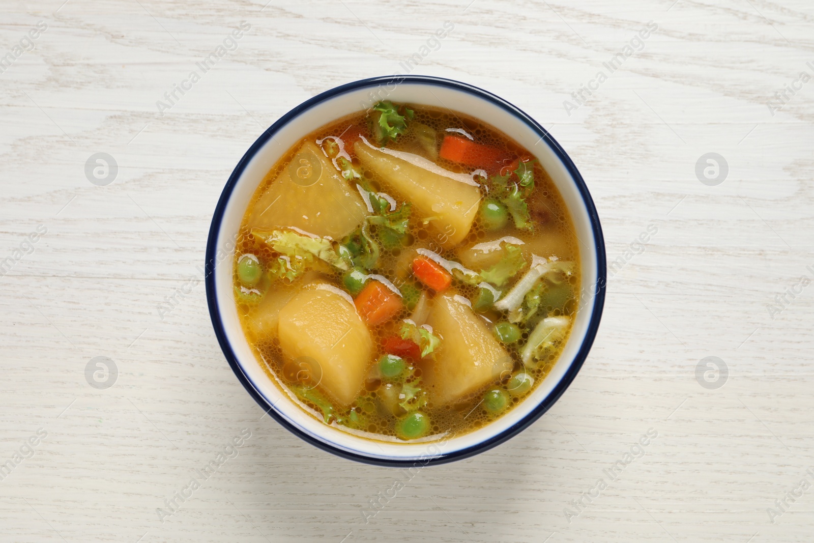 Photo of Bowl of delicious turnip soup on white wooden table, top view