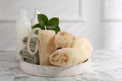 Photo of Loofah sponges, towels, green leaves and cosmetic products on white marble table