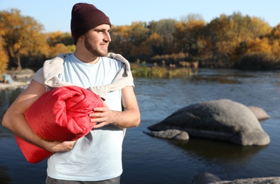 Male camper with sleeping bag near beautiful lake. Space for text