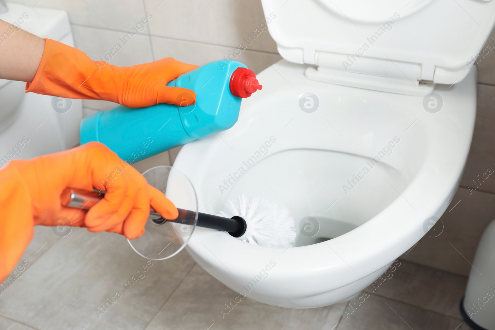 Photo of Woman in protective gloves cleaning toilet bowl with brush in bathroom, closeup