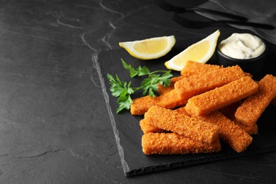 Photo of Fresh breaded fish fingers, sauce and lemon served on black table, space for text
