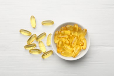 Photo of Vitamin capsules in bowl on white wooden table, top view
