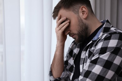 Young depressed man near window at home, space for text