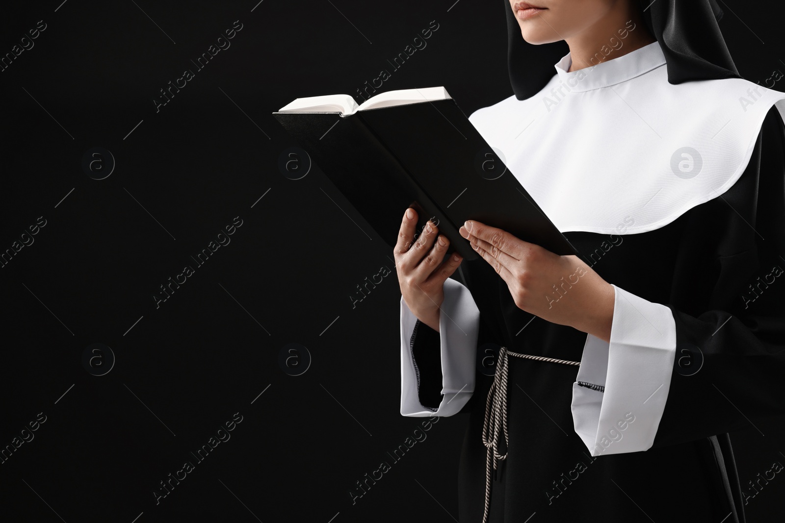 Photo of Nun reading Bible on black background, closeup. Space for text
