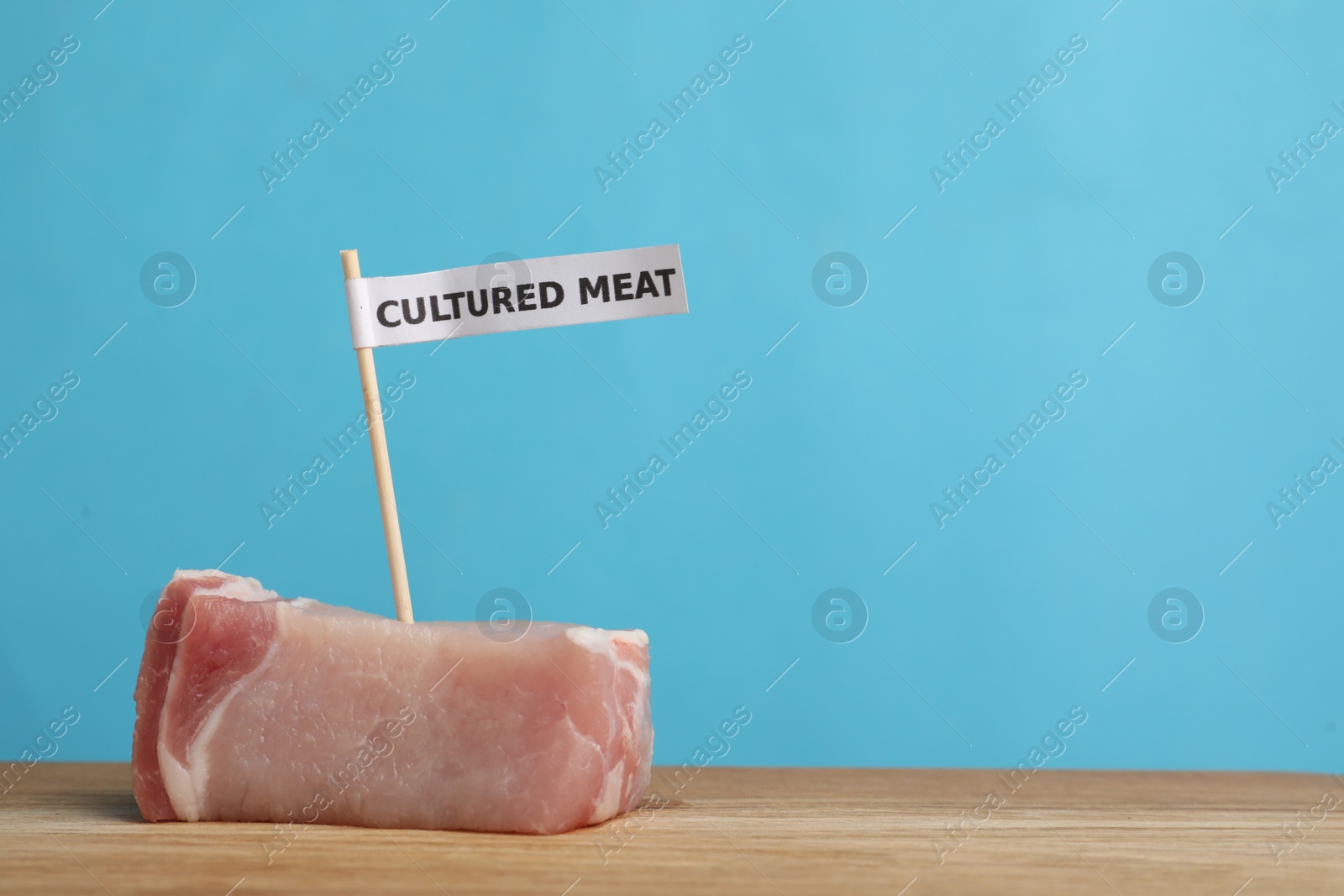 Photo of Sample of lab grown pork labeled Cultured Meat on wooden table. Space for text