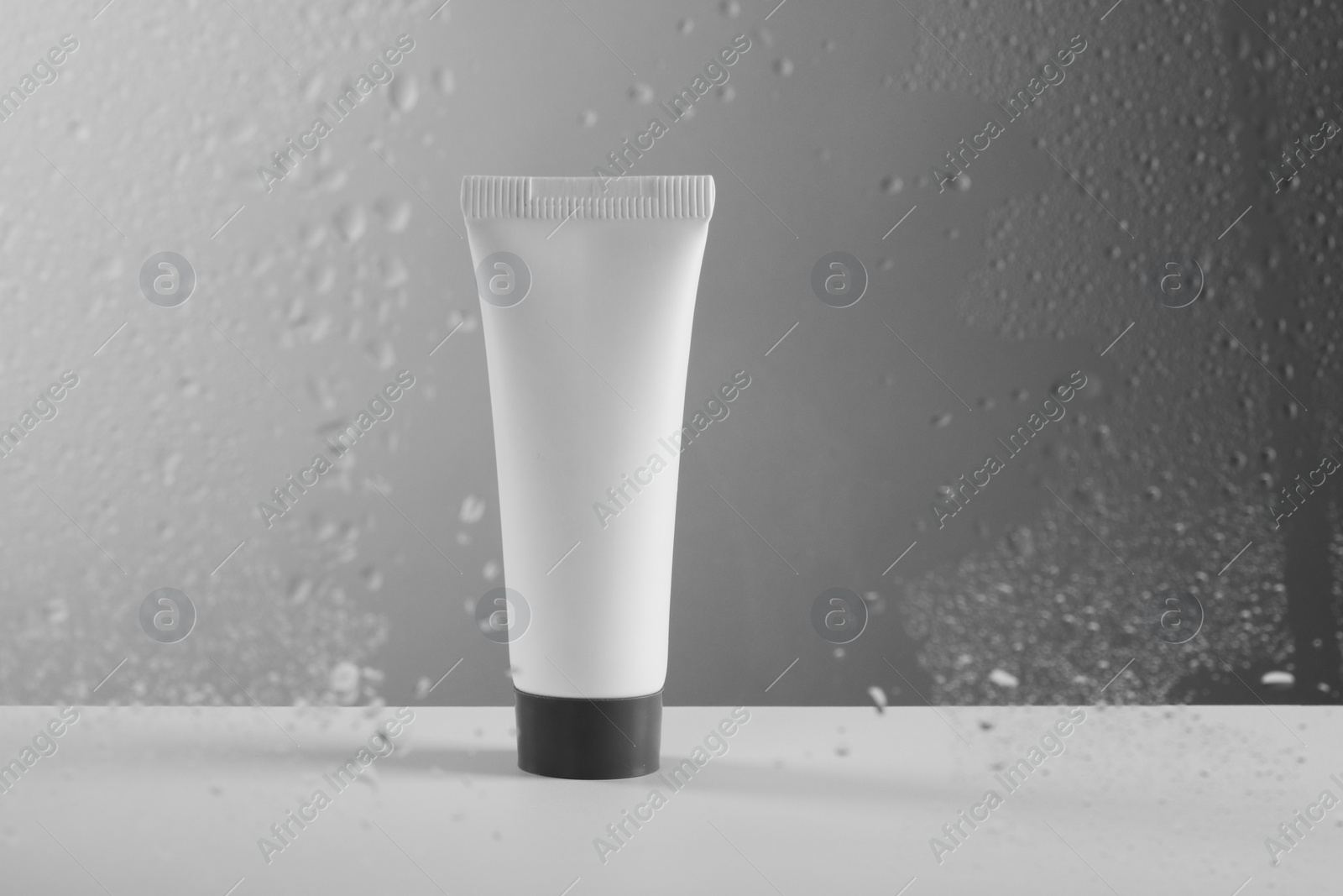 Photo of Tube with moisturizing cream on grey background, view through wet glass