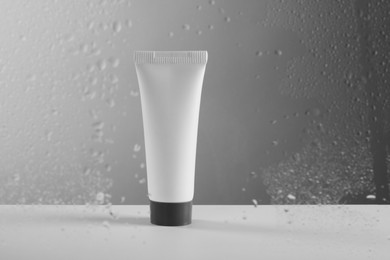 Tube with moisturizing cream on grey background, view through wet glass