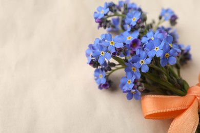 Photo of Beautiful blue forget-me-not flowers tied with ribbon on light background, closeup. Space for text