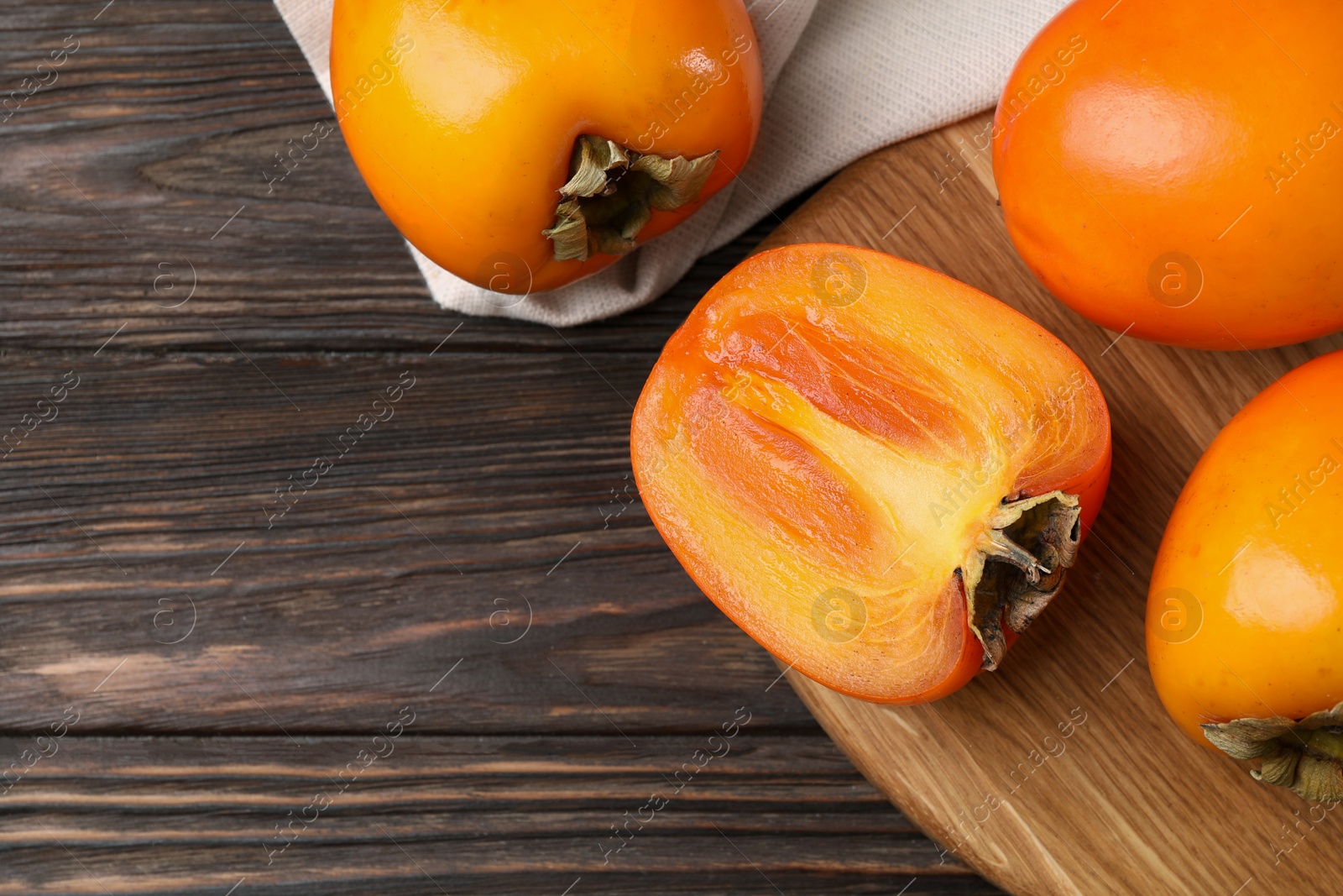 Photo of Whole and cut delicious ripe persimmons on wooden table, top view. Space for text