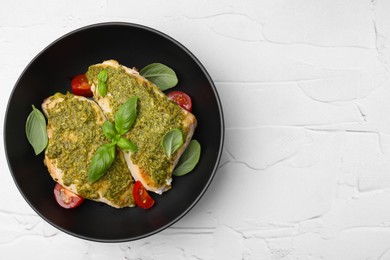 Delicious chicken breasts with pesto sauce, tomatoes and basil on white textured table, top view. Space for text