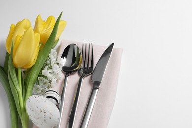 Photo of Cutlery set, Easter eggs and beautiful flowers on white background, flat lay with space for text. Festive table setting