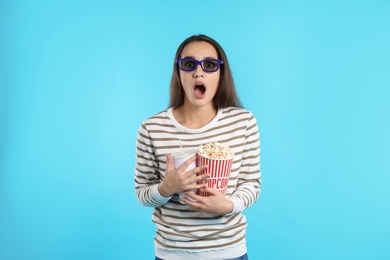 Emotional woman with 3D glasses, popcorn and beverage during cinema show on color background