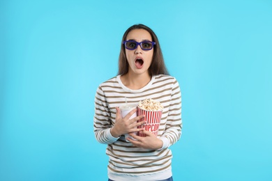 Photo of Emotional woman with 3D glasses, popcorn and beverage during cinema show on color background