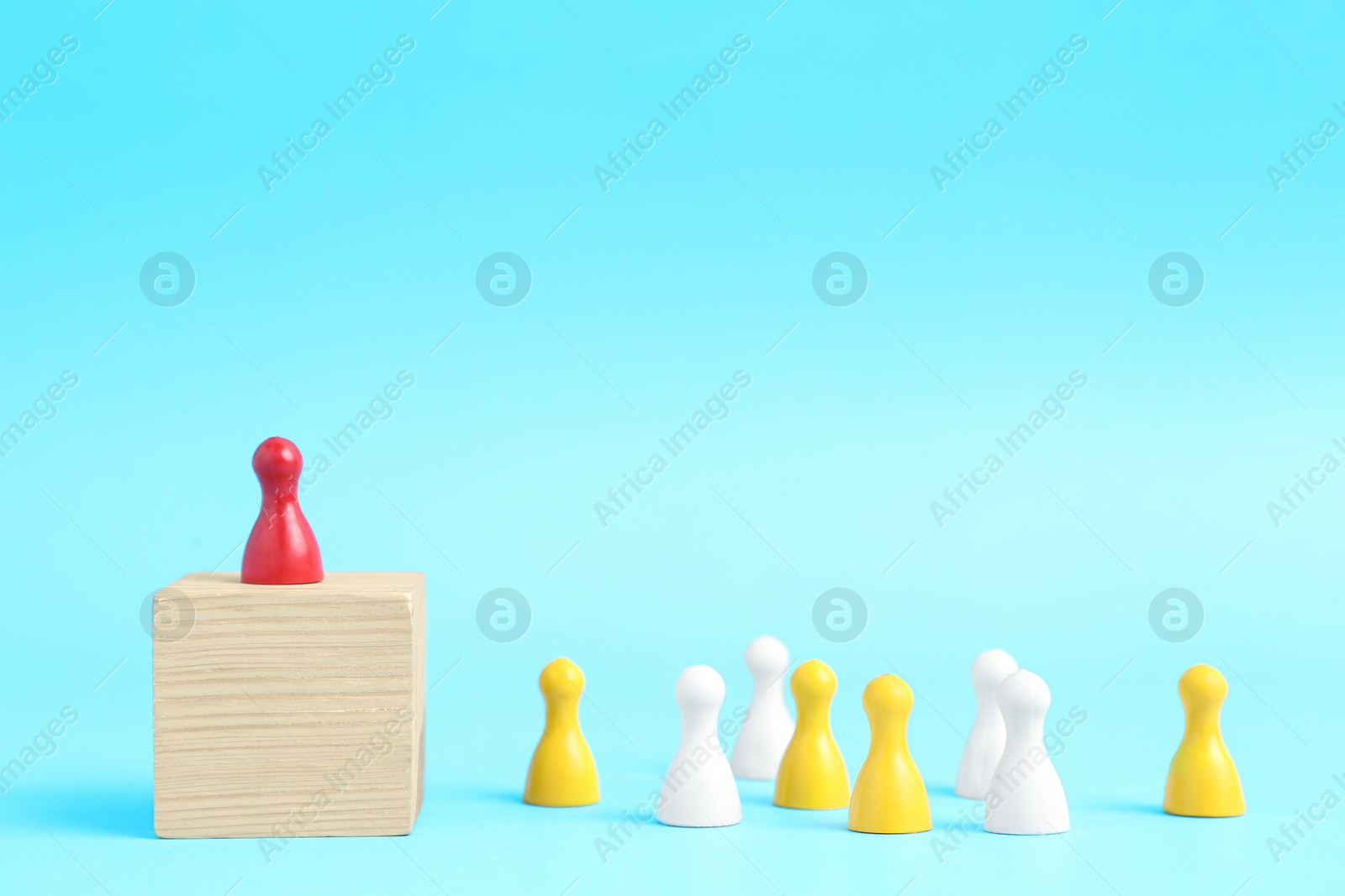 Photo of Playing pieces group and red one standing on wooden cube against light blue background, space for text. Social roles concept