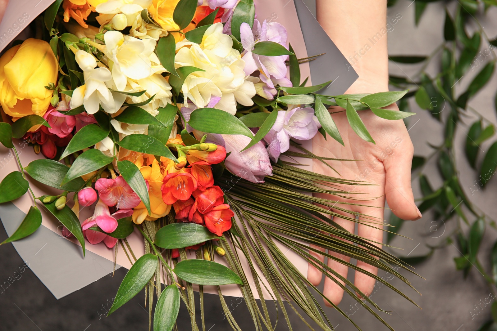 Photo of Woman with beautiful bouquet of freesia flowers on grey background