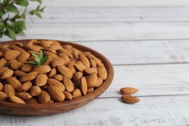 Photo of Plate with tasty almonds on white wooden table. Space for text