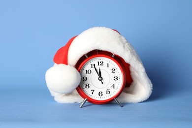 Photo of Alarm clock with Santa hat on light blue background. New Year countdown