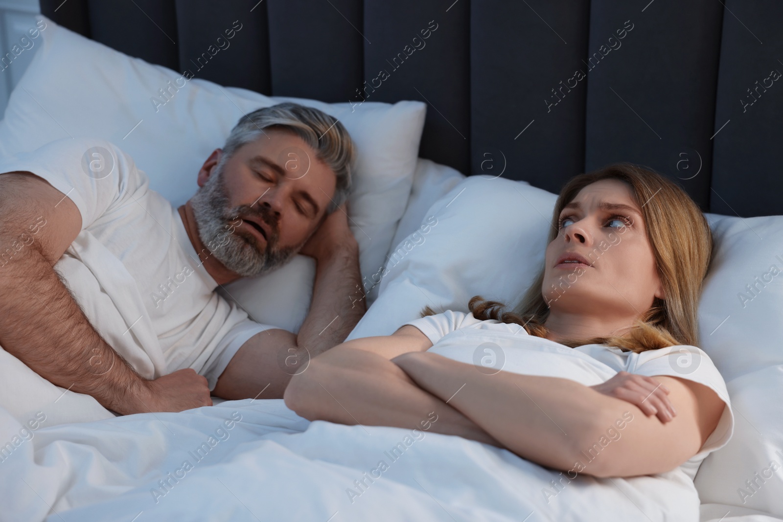 Photo of Irritated woman lying near her snoring husband in bed at home