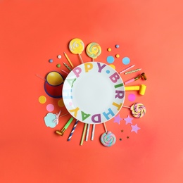 Different birthday party items and empty plate on coral background, flat lay. Space for text