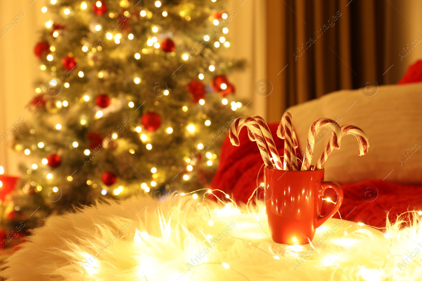 Photo of Red cup with candy canes on faux fur in room decorated for Christmas. Interior design