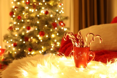 Photo of Red cup with candy canes on faux fur in room decorated for Christmas. Interior design