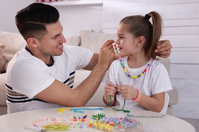 Photo of Happy father putting handmade beaded jewelry on his cute daughter at home