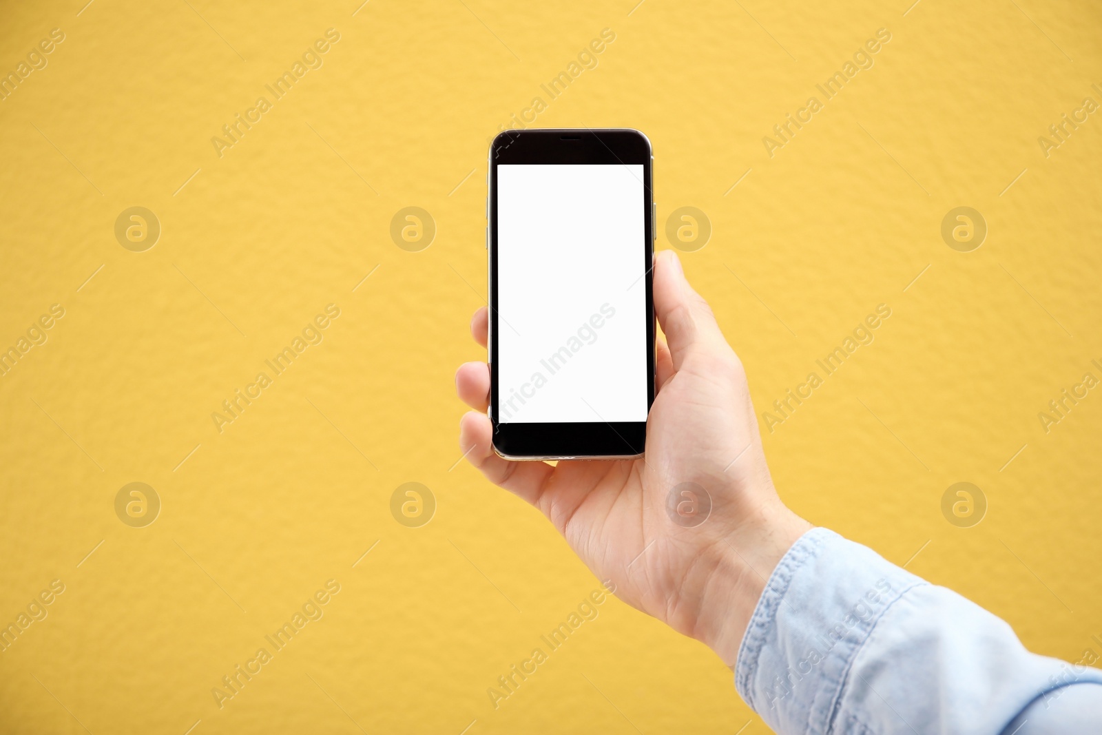 Photo of Young man holding mobile phone with blank screen in hand on color background