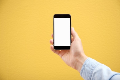Photo of Young man holding mobile phone with blank screen in hand on color background