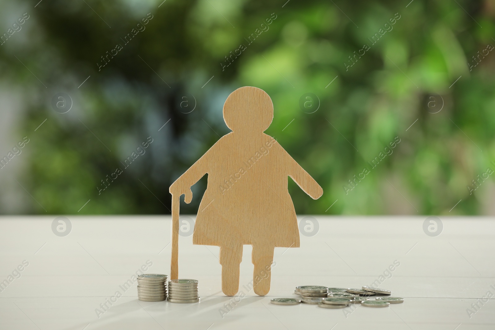 Photo of Pension savings. Figure of senior woman and coins on white table against blurred green background