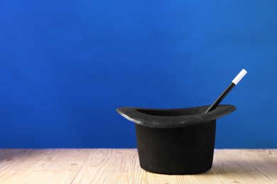 Photo of Magician's hat and wand on wooden table against blue background, space for text