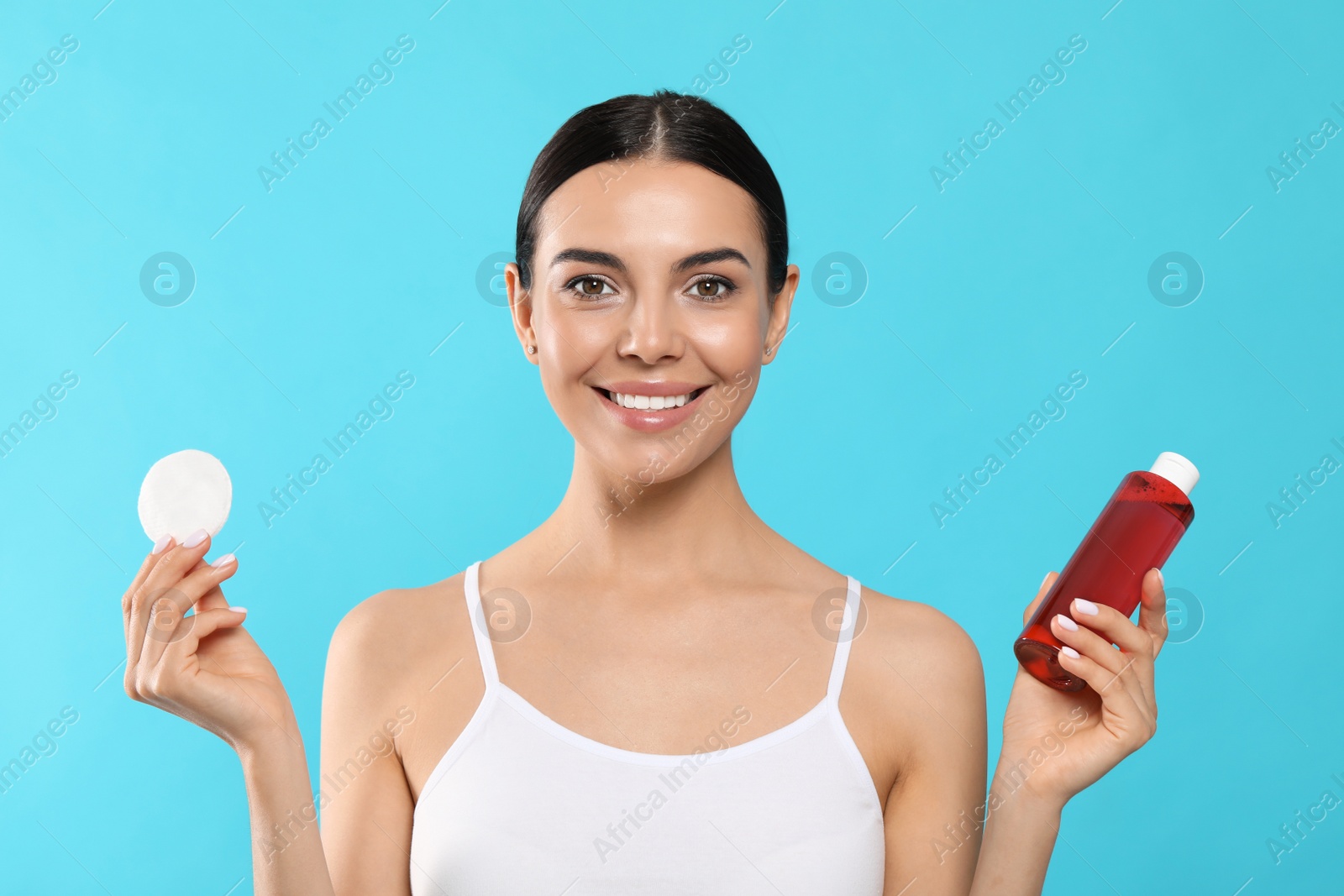 Photo of Young woman with micellar water and cotton pad on light blue background