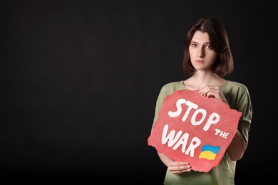 Photo of Sad woman holding poster with words Stop the War on black background. Space for text