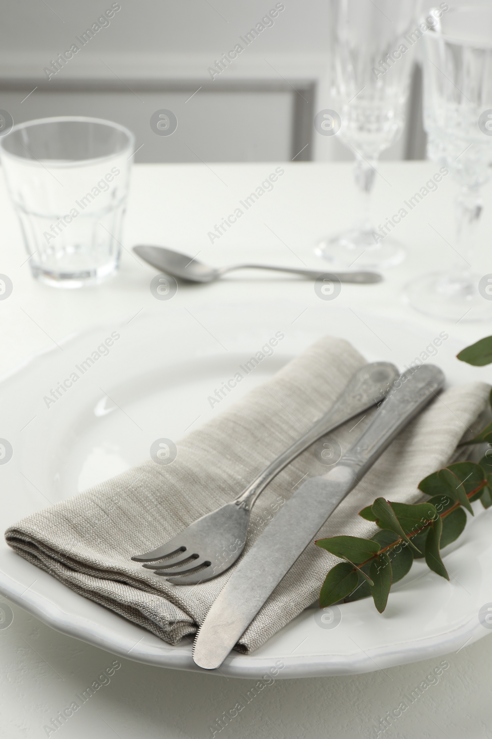 Photo of Stylish setting with cutlery, eucalyptus leaves and plate on white textured table, closeup