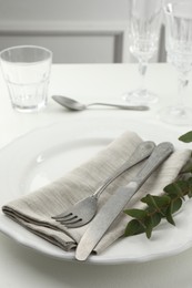 Photo of Stylish setting with cutlery, eucalyptus leaves and plate on white textured table, closeup