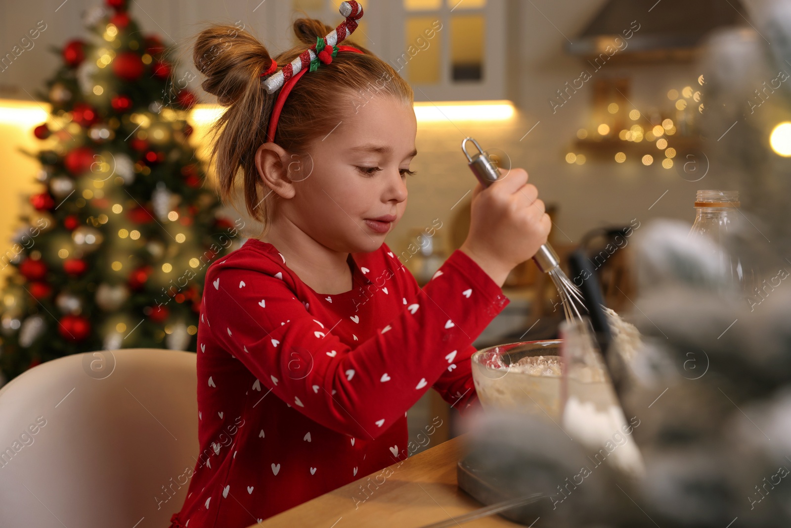 Photo of Cute little girl having fun while making dough for Christmas cookies in kitchen